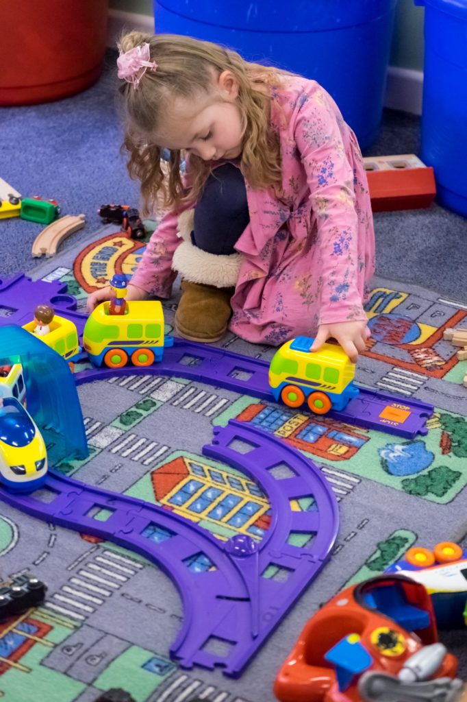 a young child playing with toy trains on a track on the nursery floor