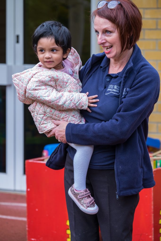 a nursery team member holding a child on her hip outside in the nursery garden